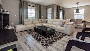A modern living room with a sectional sofa, a glass coffee table, and a dining area with a table and chairs. - 6 Bed Villa Games Pool Spa (Davenport)