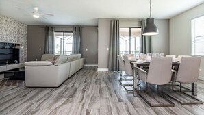 A modern living room with a sofa, dining table, and chairs. There is a ceiling fan and a pendant light above the table. - 6 Bed Villa Games Pool Spa (Davenport)