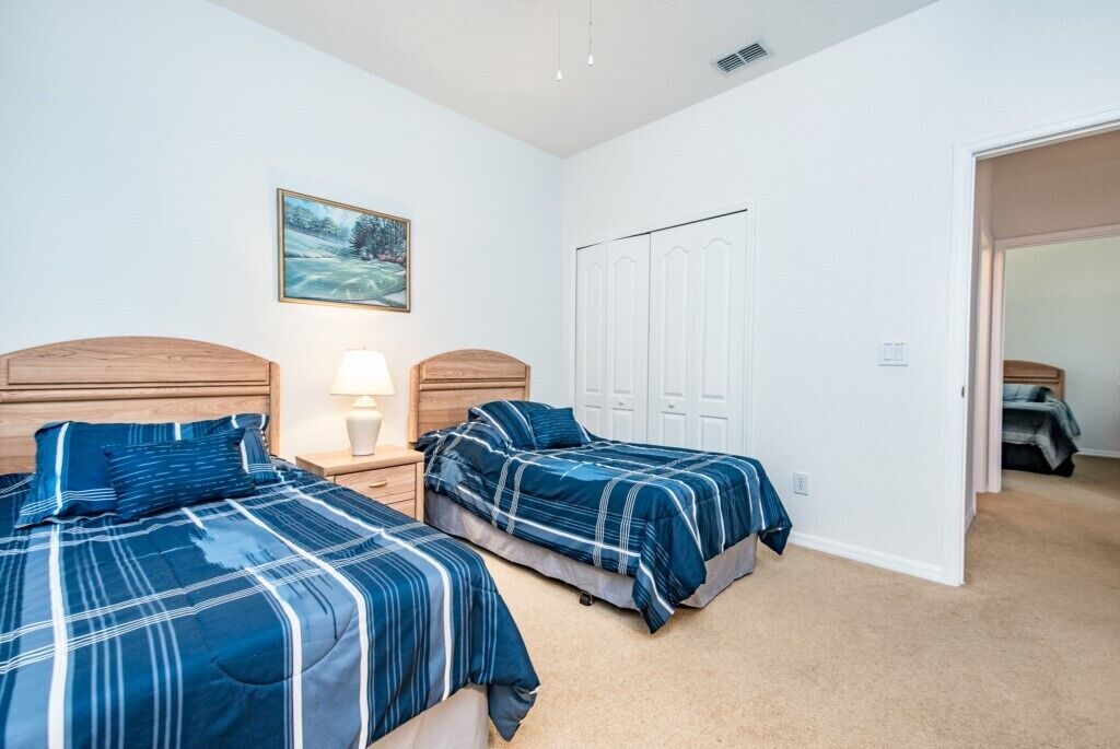 Een slaapkamer met twee bedden, een nachtkastje met een lamp, een kledingkast en een schilderij aan de muur.
