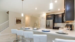 A modern kitchen with dark cabinets, a white countertop, and a bar area with white stools. - 1586sandb (Davenport)