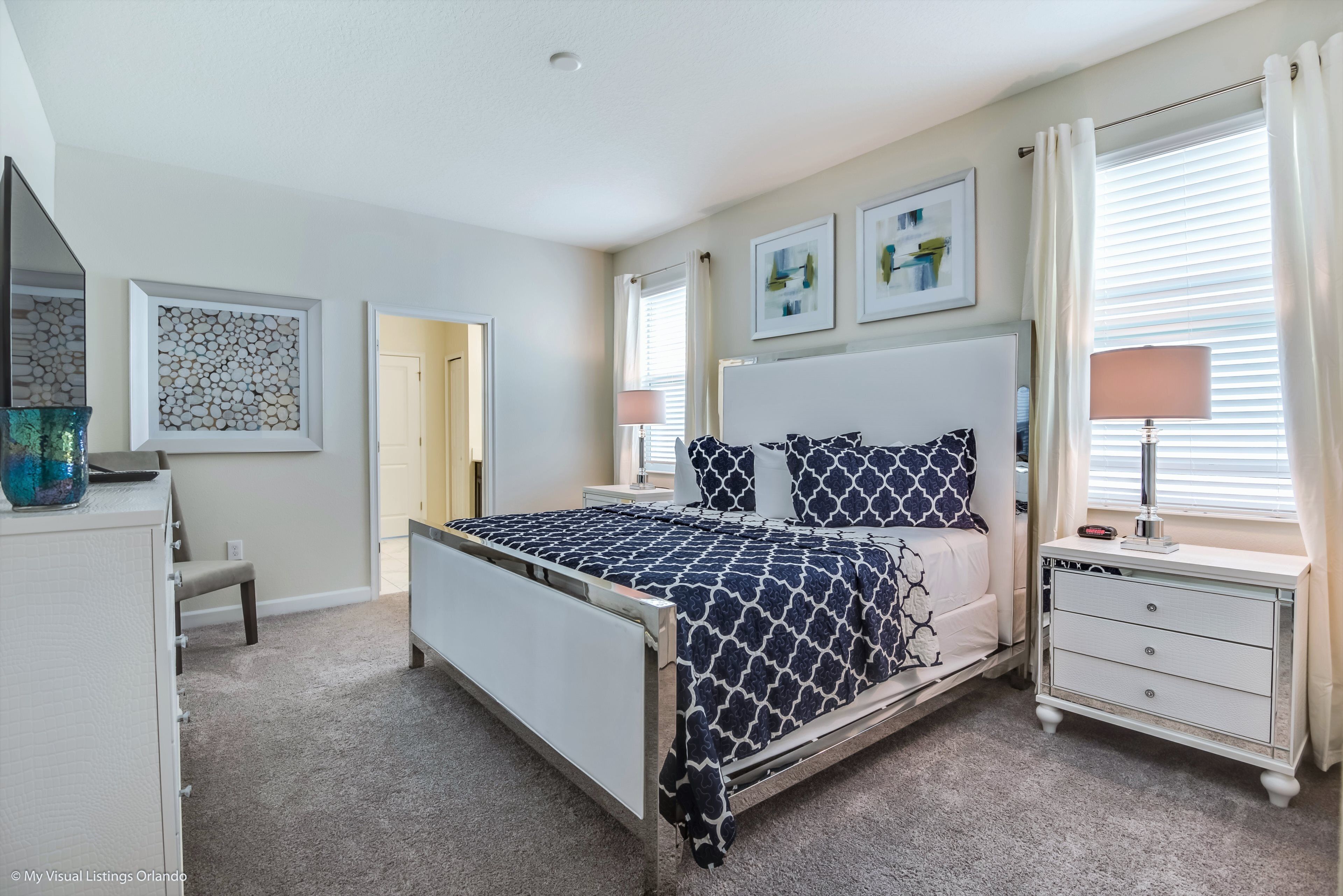 A bedroom with a bed, bedside tables, a dresser, and artwork on the walls.