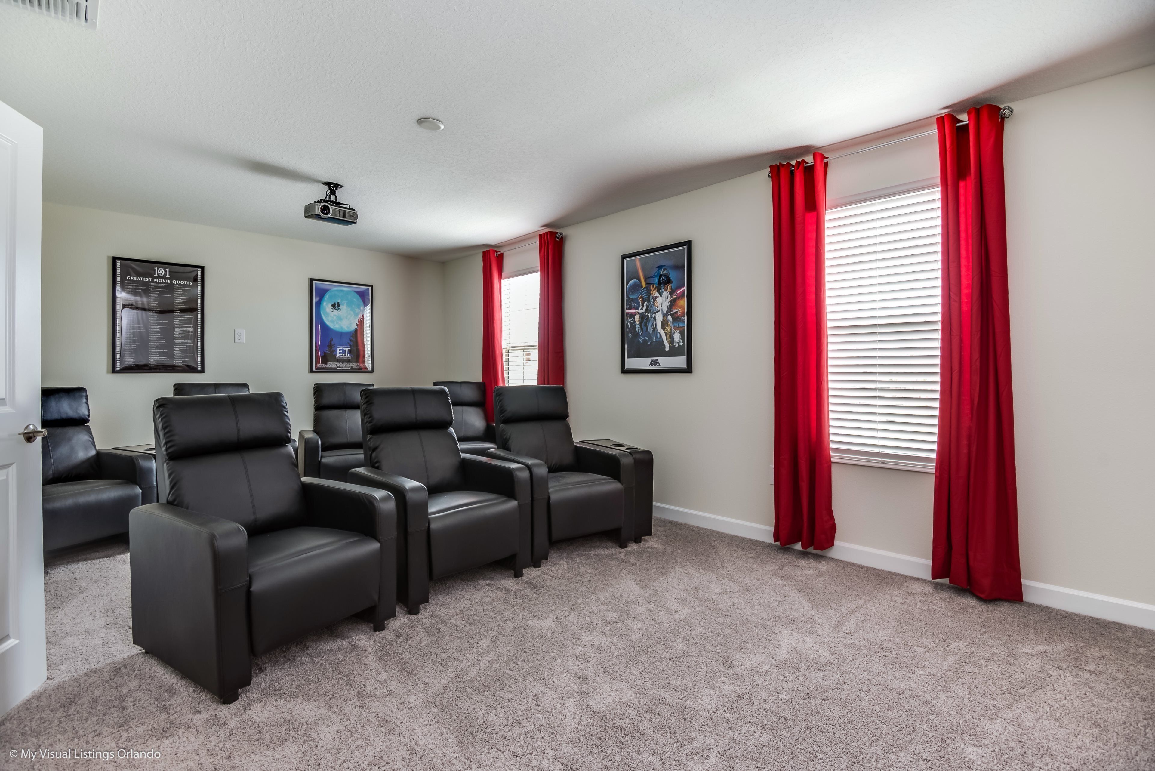 A home theater room with four black leather recliners, red curtains, and a projector on the ceiling.