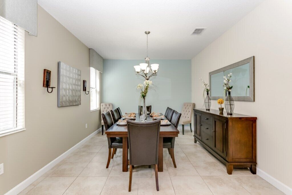 Uma sala de jantar com uma mesa posta para quatro pessoas, rodeada por cadeiras, um lustre e um armário com objetos decorativos.