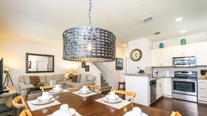 A dining area with a wooden table set for four, a kitchen with white cabinets and stainless steel appliances, and a living room with a sofa and a coffee table.
