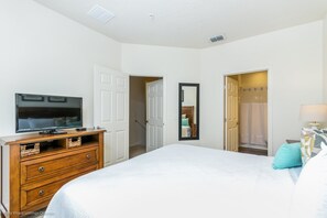 A bedroom with a bed, a TV on a dresser, a mirror, and a door leading to a bathroom. - Lucaya Village Resort 4 Bdrm (Lake Buena Vista)