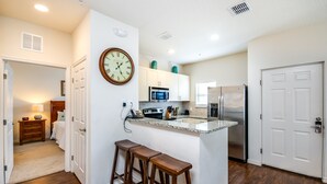 A kitchen with a central island, wooden stools, a clock, and white cabinets.