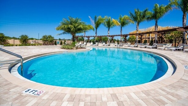 A circular pool with lounge chairs and palm trees, surrounded by a tiled deck.