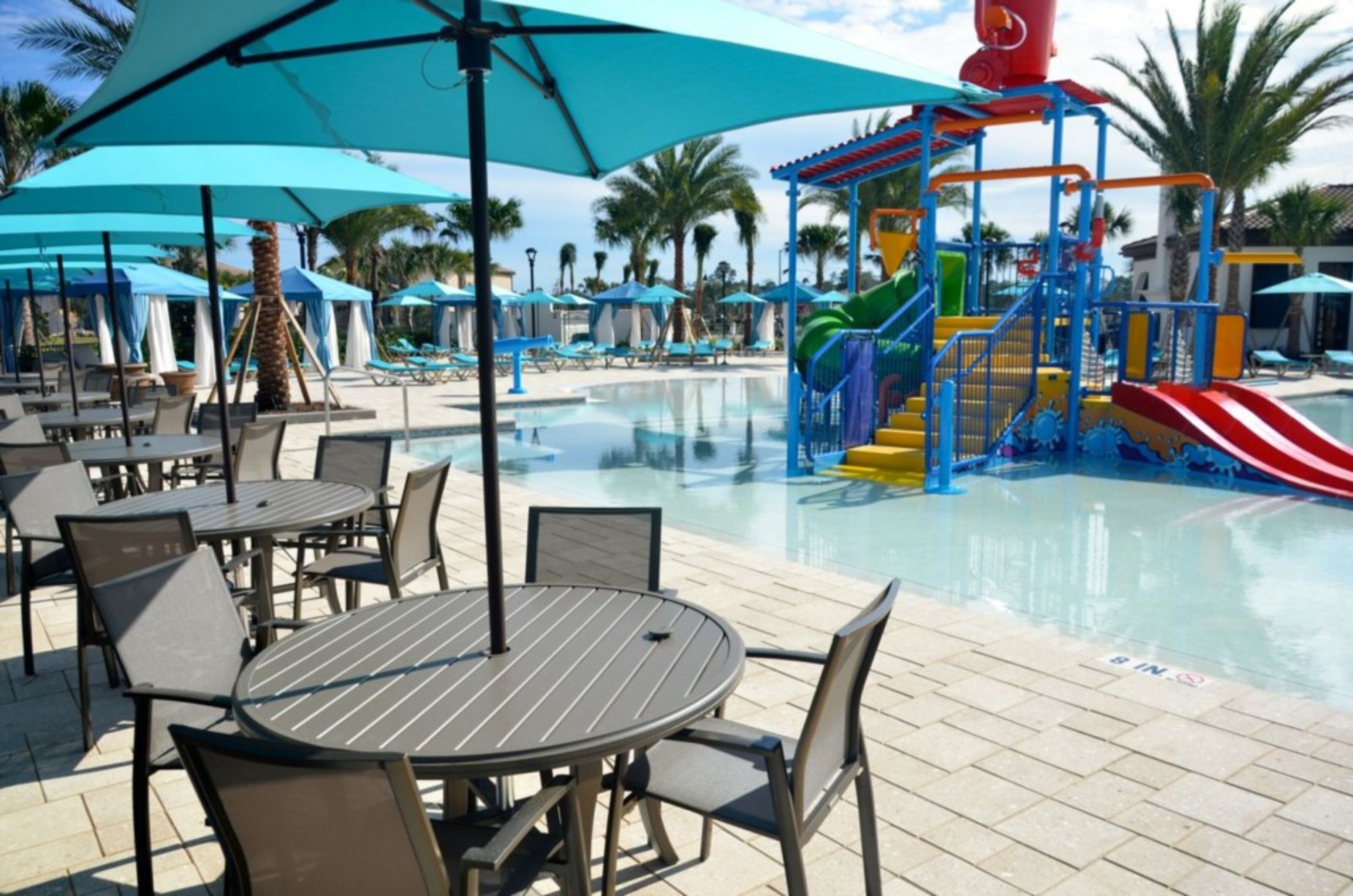 Un espace piscine équipé de chaises longues et de parasols, d’un toboggan et d’une aire de jeux.
