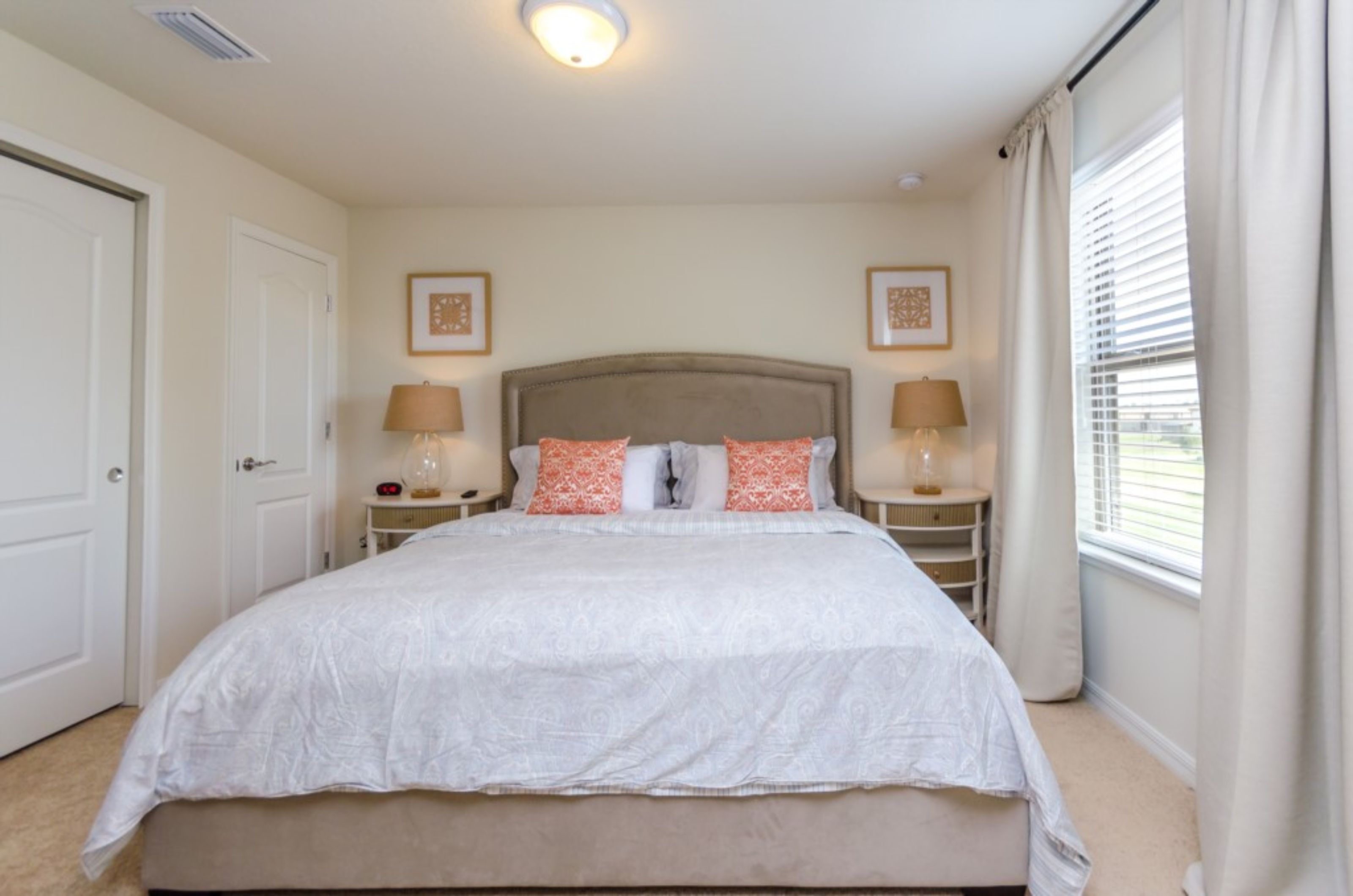 A bedroom with a large bed, two bedside tables with lamps, a headboard, and framed pictures on the wall.