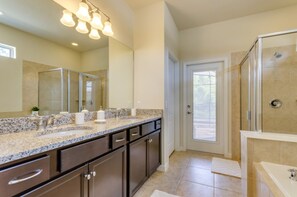 Un baño moderno con lavamanos de granito, muebles oscuros, un espejo grande y cabina de ducha de vidrio.