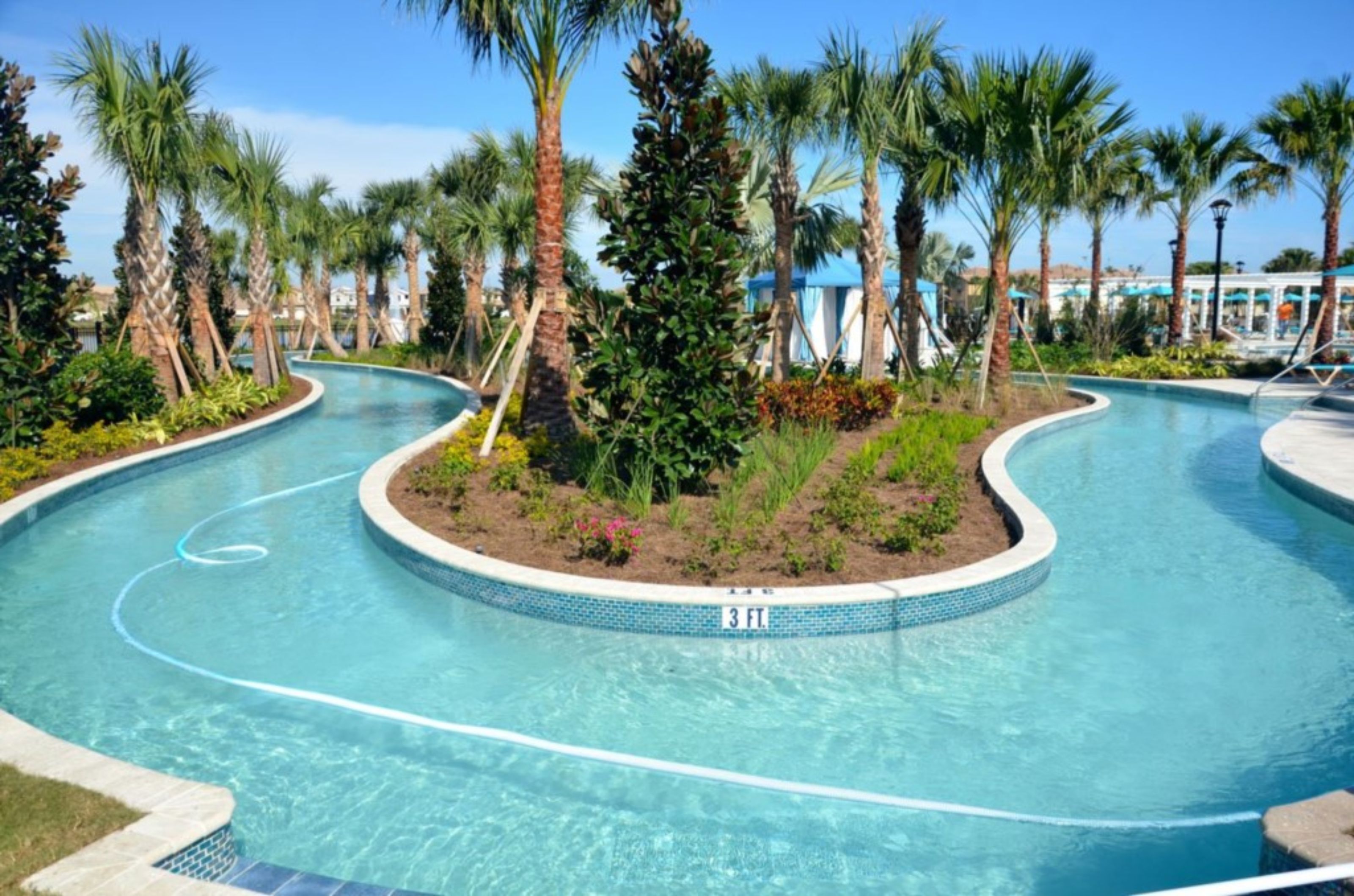 A swimming pool with a 3 ft. depth marker, surrounded by palm trees and a landscaped garden.