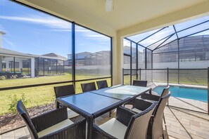 A covered patio area with a glass table and wicker chairs, overlooking a swimming pool and a grassy yard. - 7 BD 5 BH Villa Game, Pool and Spa (Kissimmee)