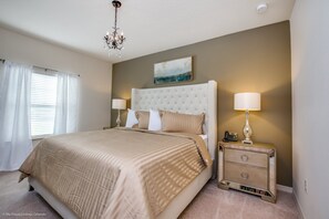 A bedroom with a large bed, two bedside lamps, a nightstand, and a chandelier. - 3 Bdrm West Lucaya Village (Kissimmee)