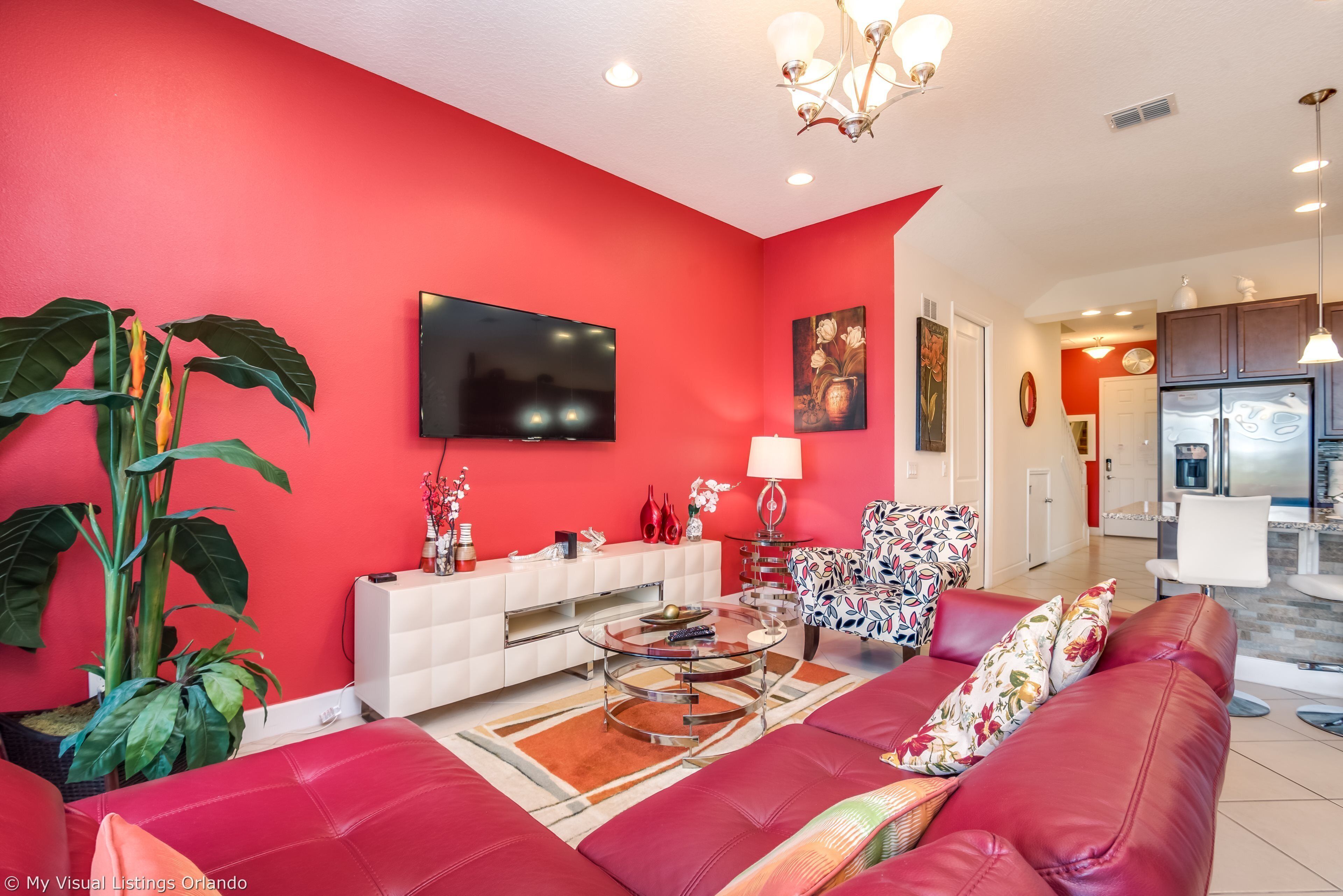 Una sala de estar moderna con una pared roja, un televisor de pantalla plana, un sofá, una mesa de centro y una planta grande.