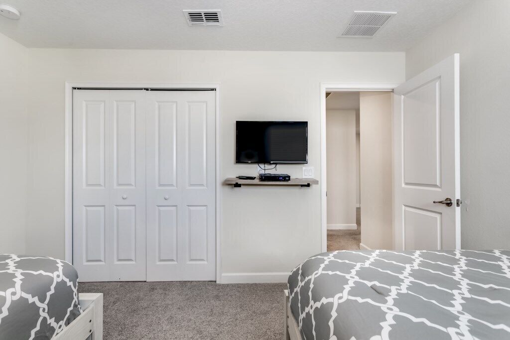 A bedroom with two beds, a TV on a shelf, and a closet.
