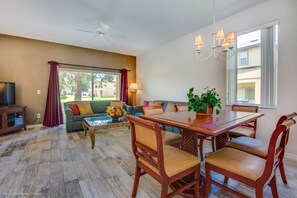 Amplia sala de estar con una mesa de comedor de madera, asientos cómodos, televisor y un ventanal con cortinas.