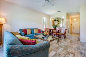 A living room with a blue sofa, a glass coffee table, and a dining area with wooden chairs and a table. - 2735calab (Davenport)