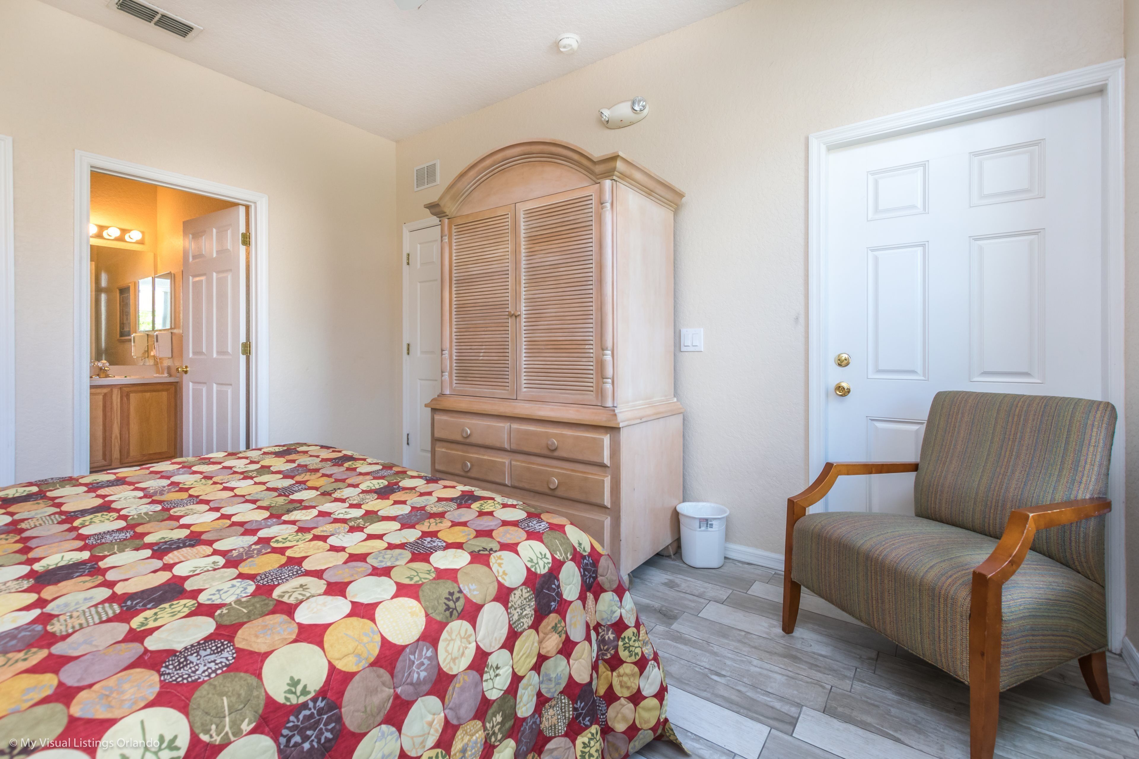 A bedroom with a bed, a wooden armoire, a chair, and a door.
