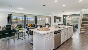 Uma sala de estar ampla com cozinha central grande, móveis modernos e vista para o exterior.