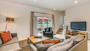 A modern living room with a sofa, armchair, coffee table, TV, and a sliding glass door leading to an outdoor area.