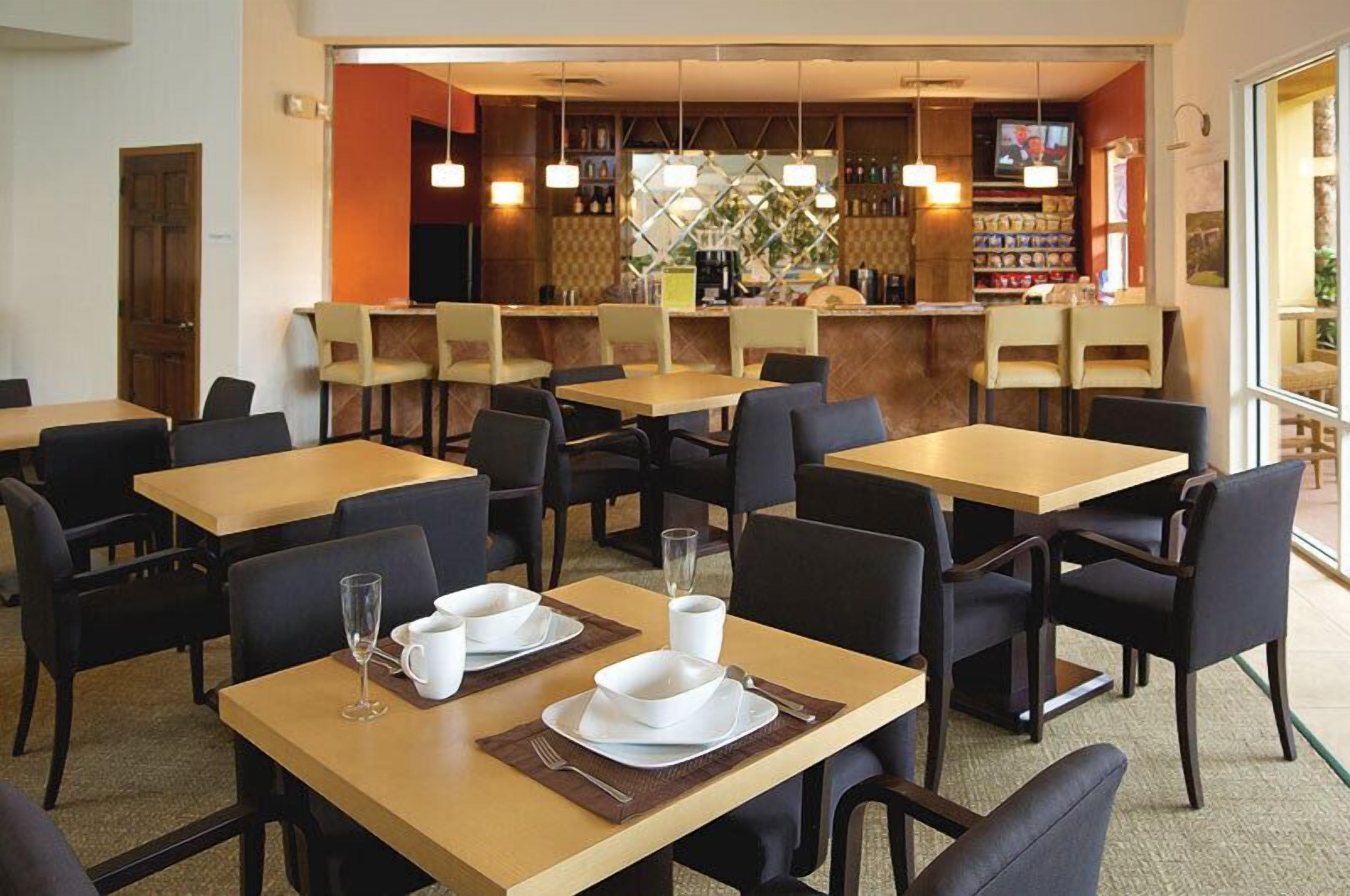 Un restaurant doté de nombreuses tables et chaises, un bar avec des étagères remplies de bouteilles et un écran de télévision.