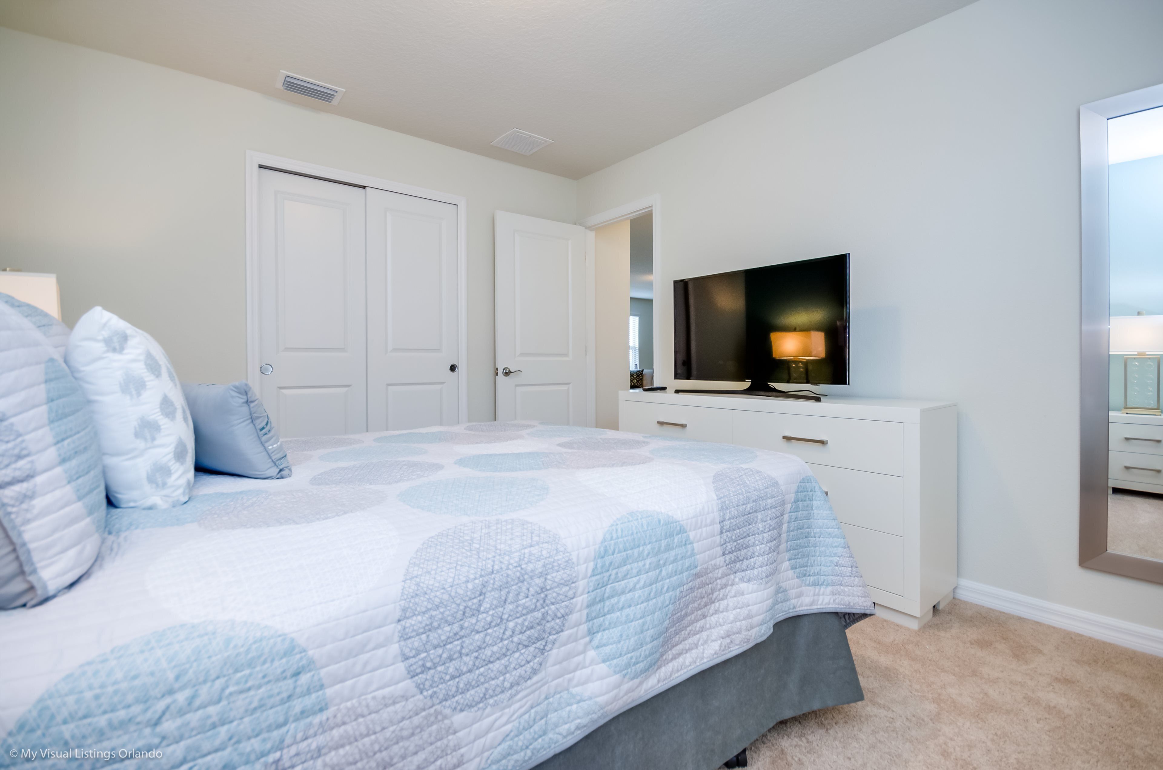 A bedroom with a bed, a TV, a dresser, and a door.