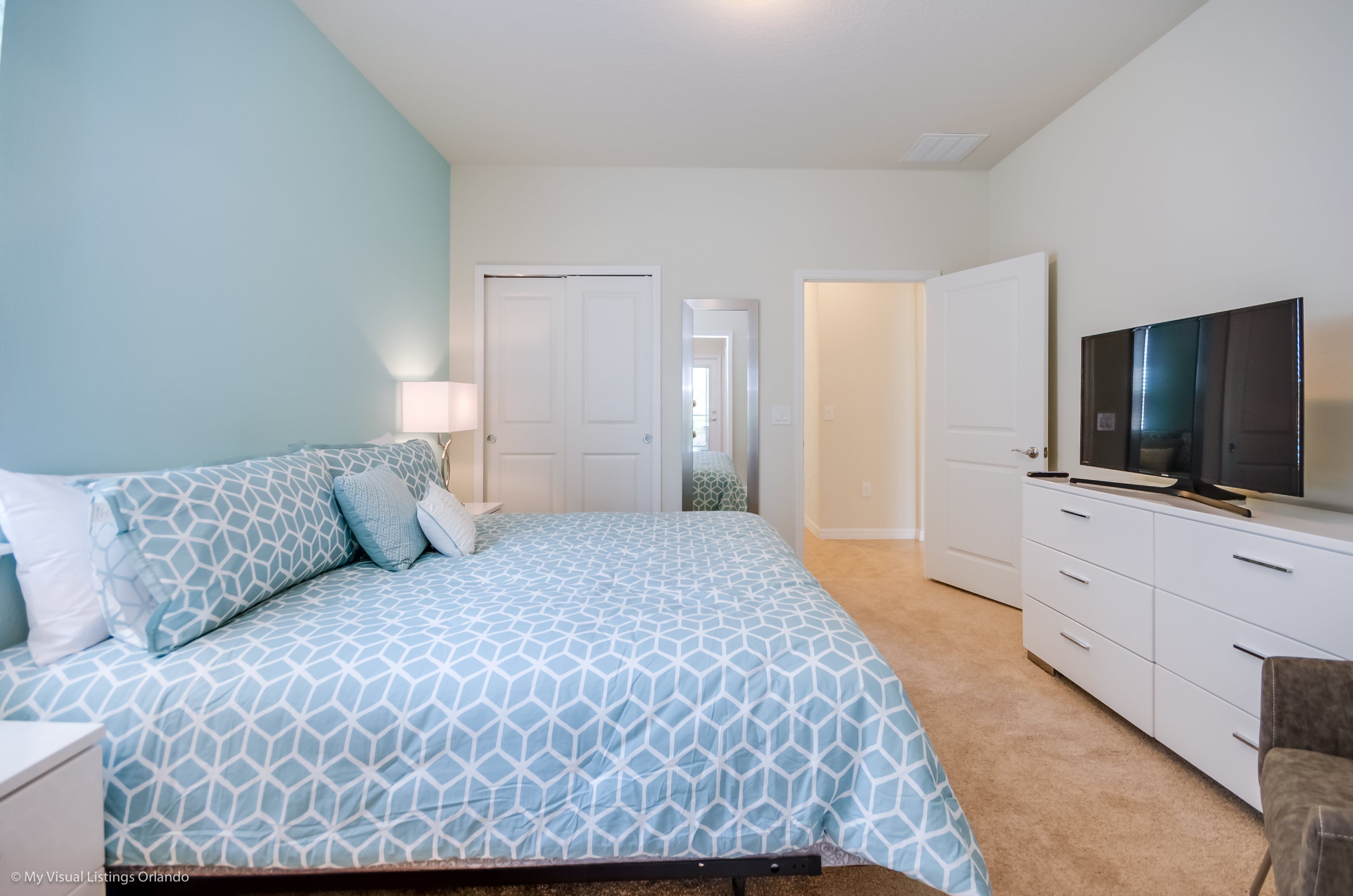 A bedroom with a bed, a TV, a dresser, and a door leading to another room.