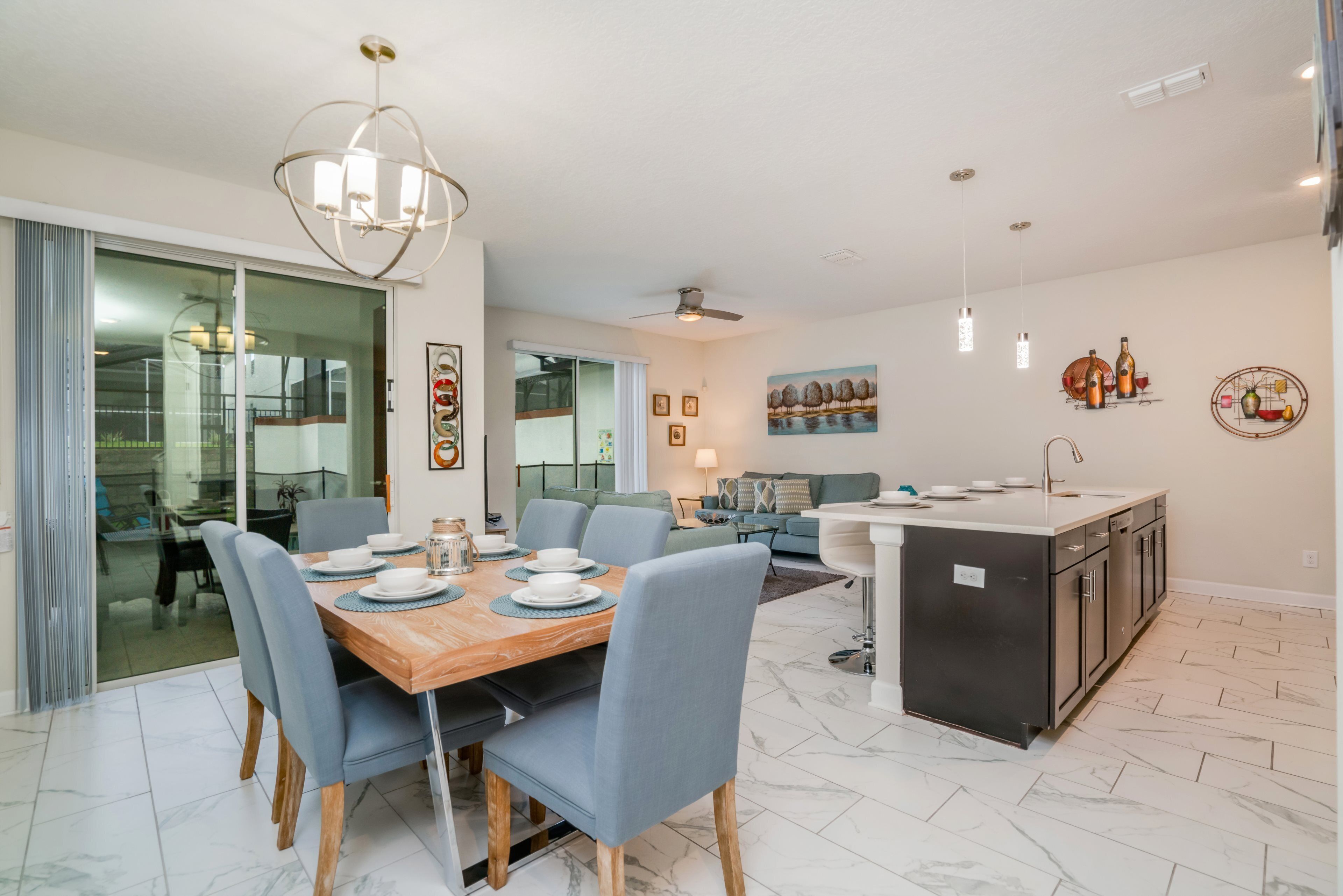 A modern kitchen with a central island, a dining area with a wooden table and blue chairs, and a living area with a sofa and a coffee table.