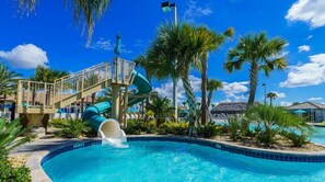 A pool with a water slide, palm trees, and a thatched-roof building.