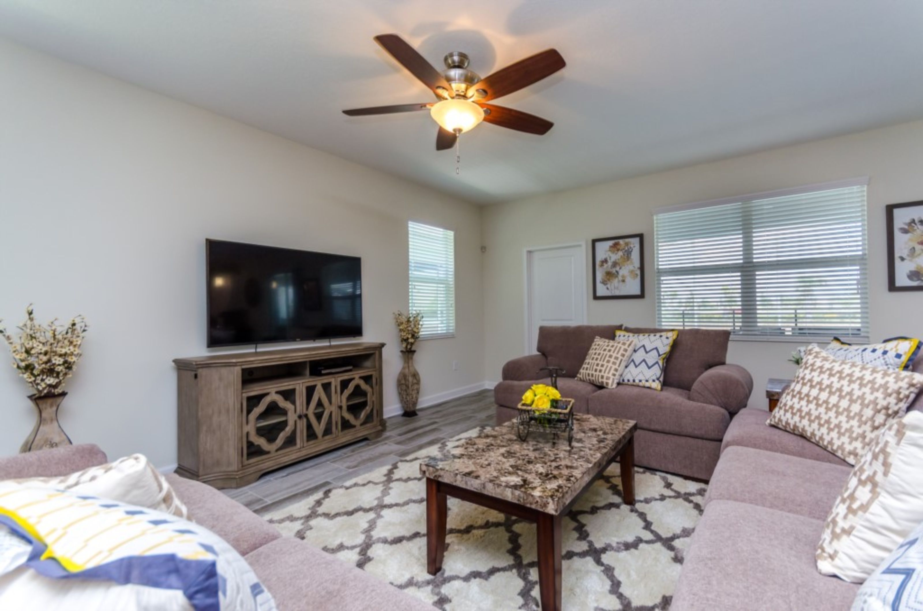 A living room with a flat-screen TV, a ceiling fan, a sofa set, and a coffee table.