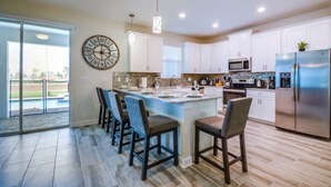 A modern kitchen with a central island, bar stools, white cabinets, stainless steel appliances, and a large wall clock. - 6 Bedroom 5 Bathroom (Davenport)