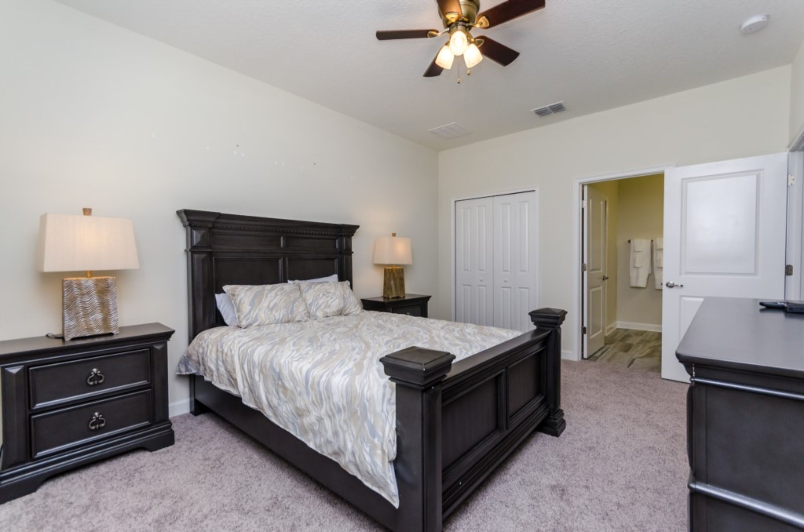 A bedroom with a dark wood bed, two bedside tables with lamps, a ceiling fan, and a white door leading to another room.