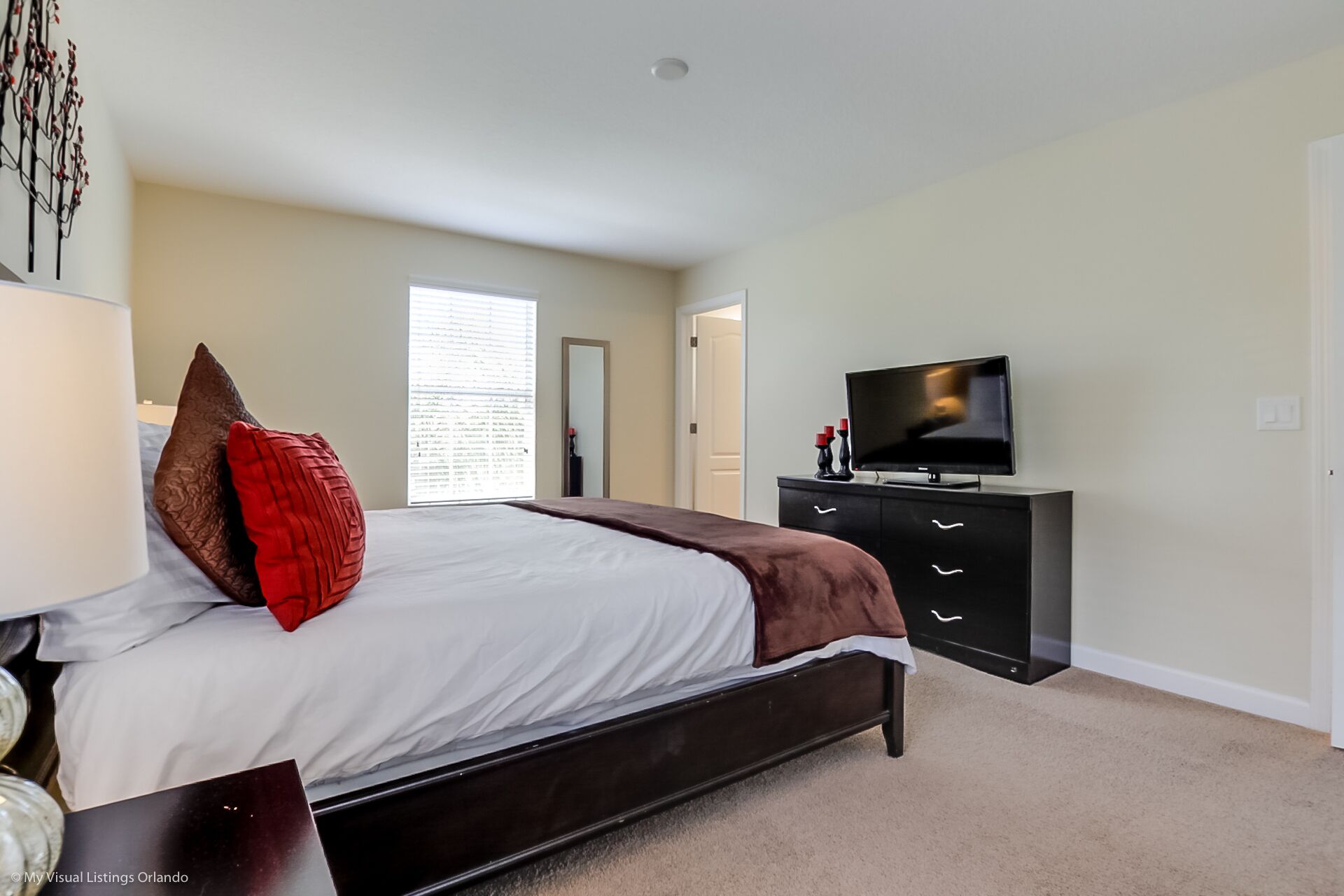 Une chambre à coucher comprenant un lit, une commode, un téléviseur et une fenêtre avec des stores.