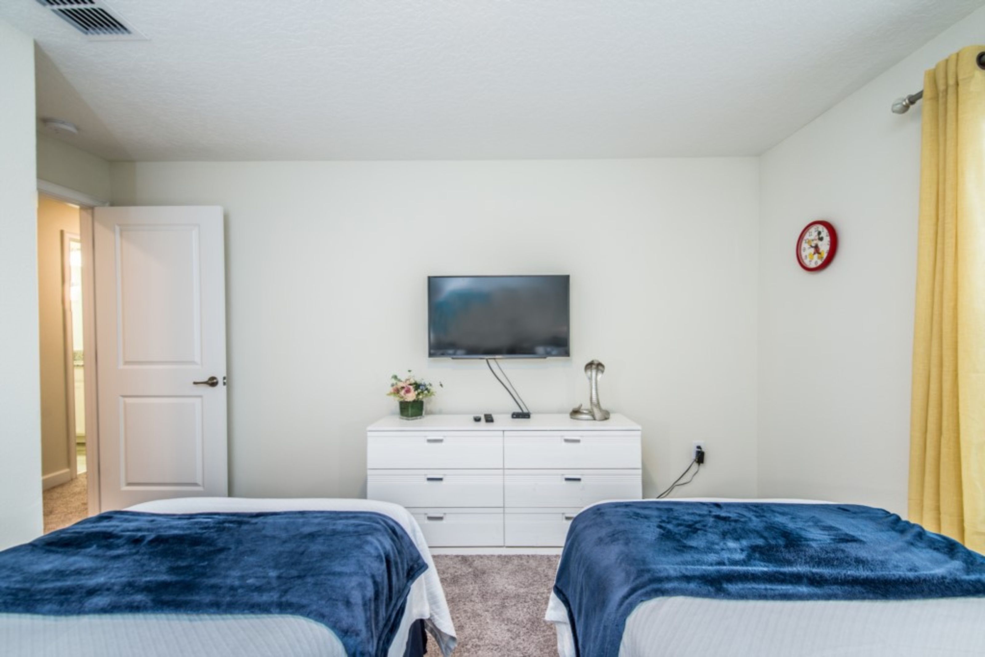Un dormitorio con dos camas, un aparador, un televisor en la pared y un reloj.