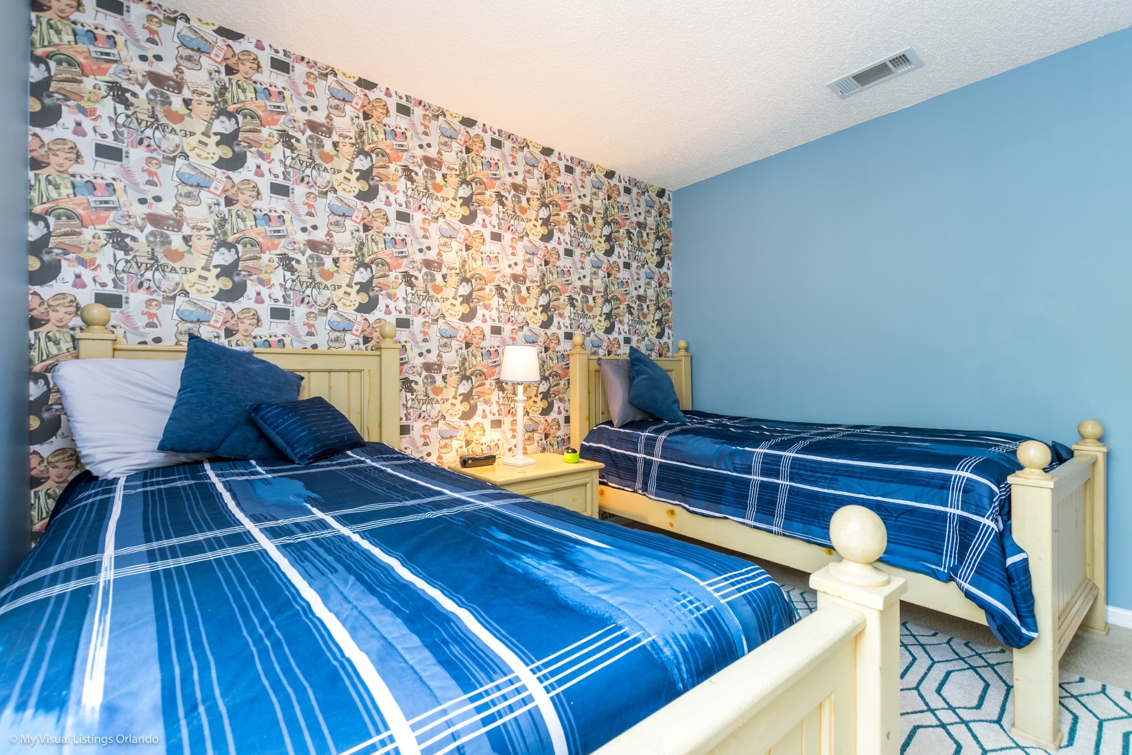 A bedroom with two beds, a patterned wallpaper, and a blue wall.