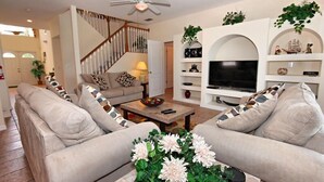 Uma sala de estar com sofá, mesa de centro, televisão e objetos decorativos.
