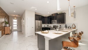 A modern kitchen with dark cabinets, stainless steel appliances, and a central island with bar stools. - 8 Bdrm Champions Gate Villa (Kissimmee)