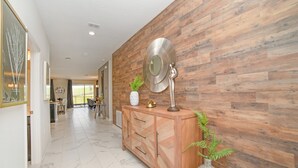 A hallway with a wooden wall, a marble floor, a wooden cabinet with a mirror, and a potted plant. - 8 Bdrm Champions Gate Villa (Kissimmee)