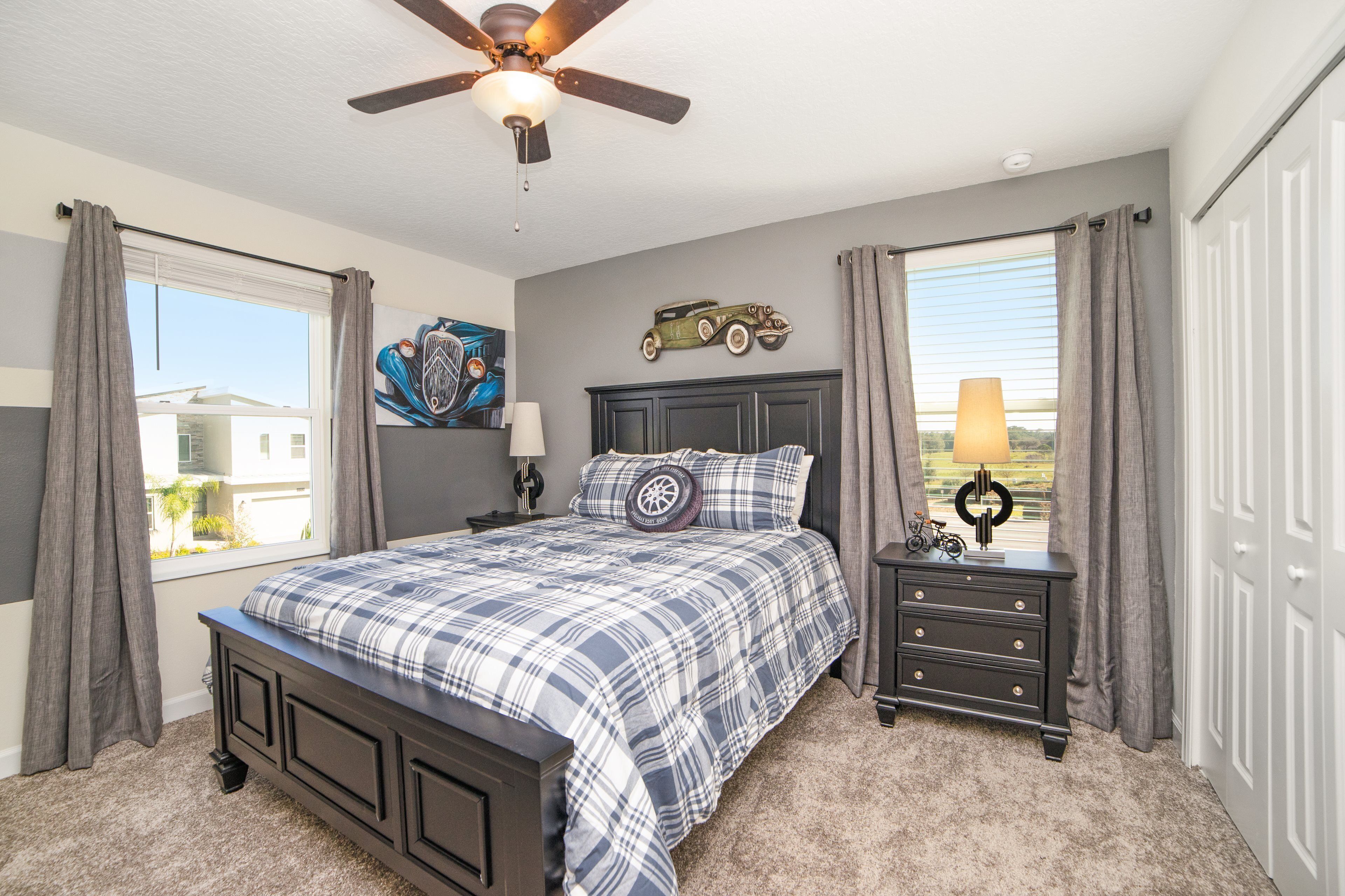 A bedroom with a bed, nightstands, a ceiling fan, a window with curtains, and a wall-mounted decoration.