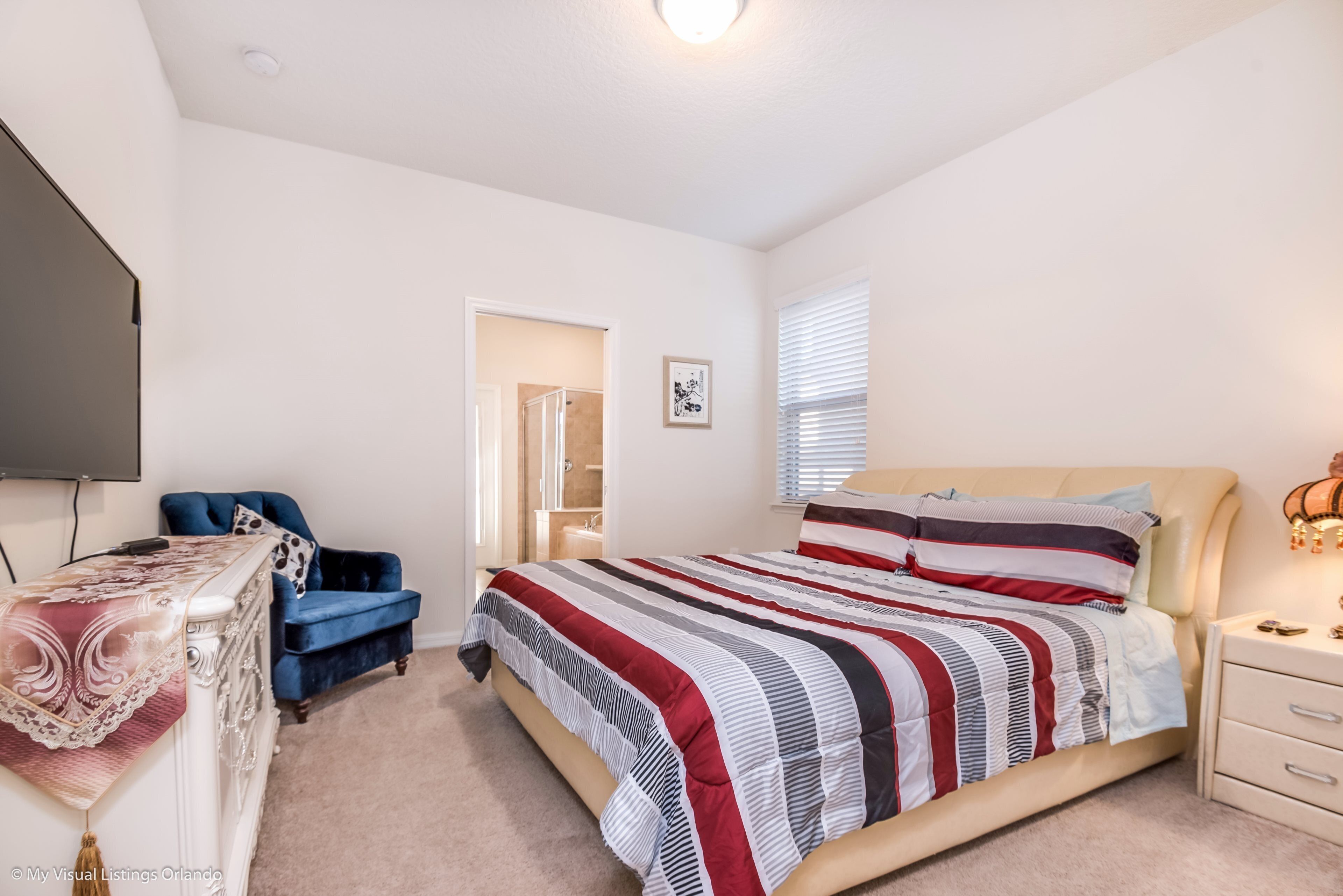 A bedroom with a bed, a desk, a chair, and a TV.