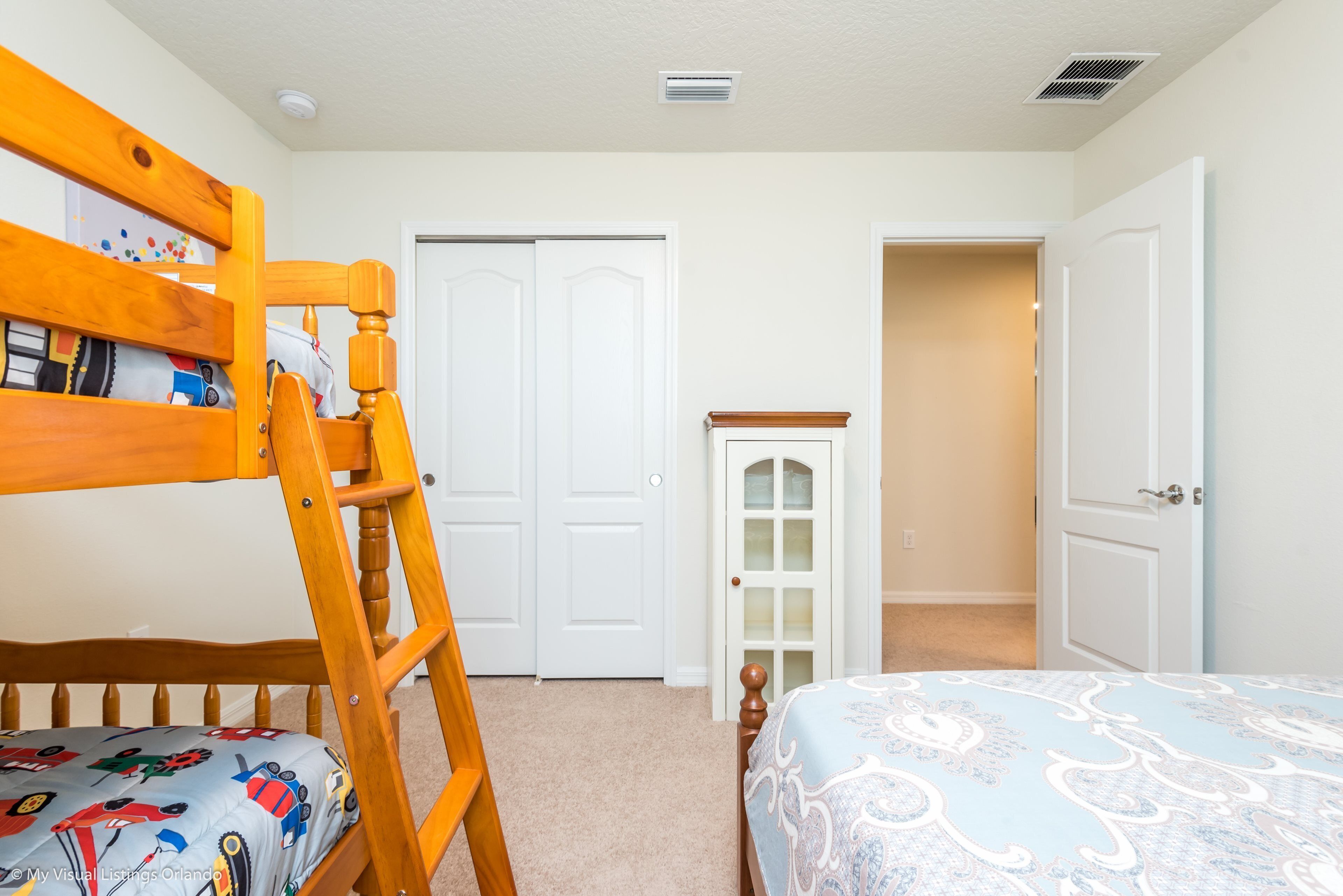 A bedroom with a bunk bed, a wooden ladder, a closet, and a door leading to another room.