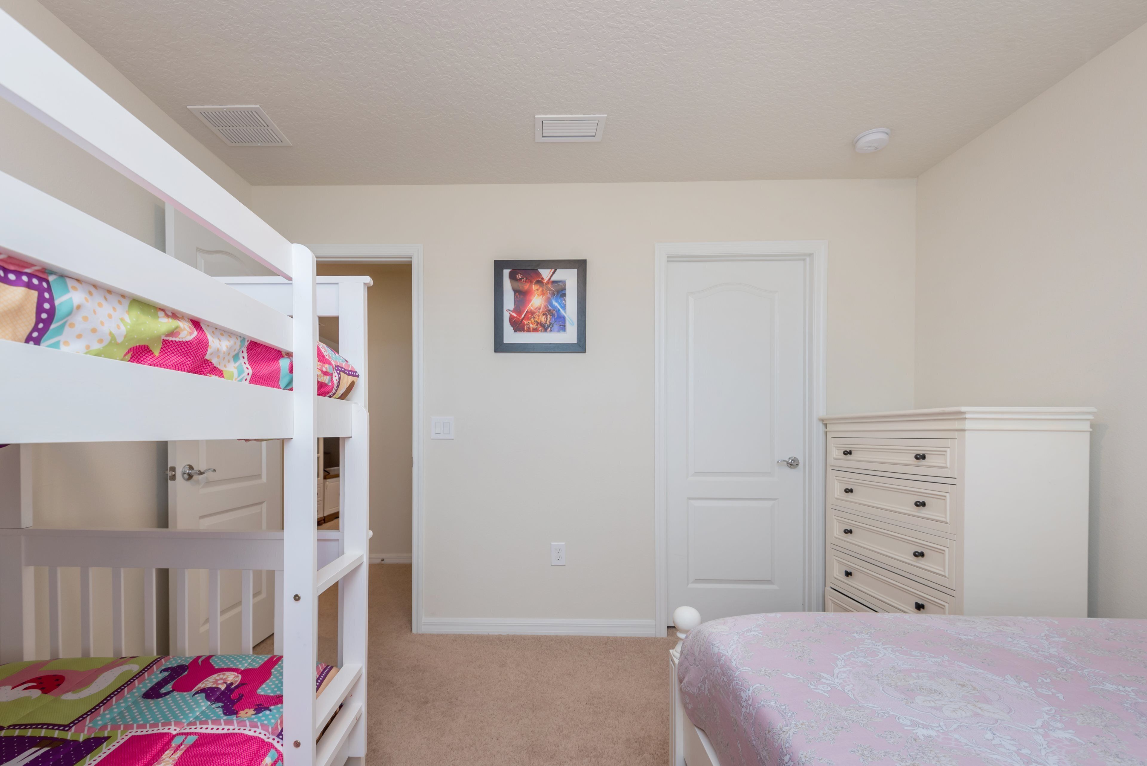 A bedroom with bunk beds, a dresser, a door, and a framed picture on the wall.