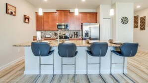 A modern kitchen with wooden cabinets, stainless steel appliances, and a bar area with three bar stools. - 4bed 3Ba Champions Gate Pool Home (Davenport)