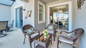A patio area with wicker furniture, a glass table, and a vase of flowers. - 4bed 3Ba Champions Gate Pool Home (Davenport)