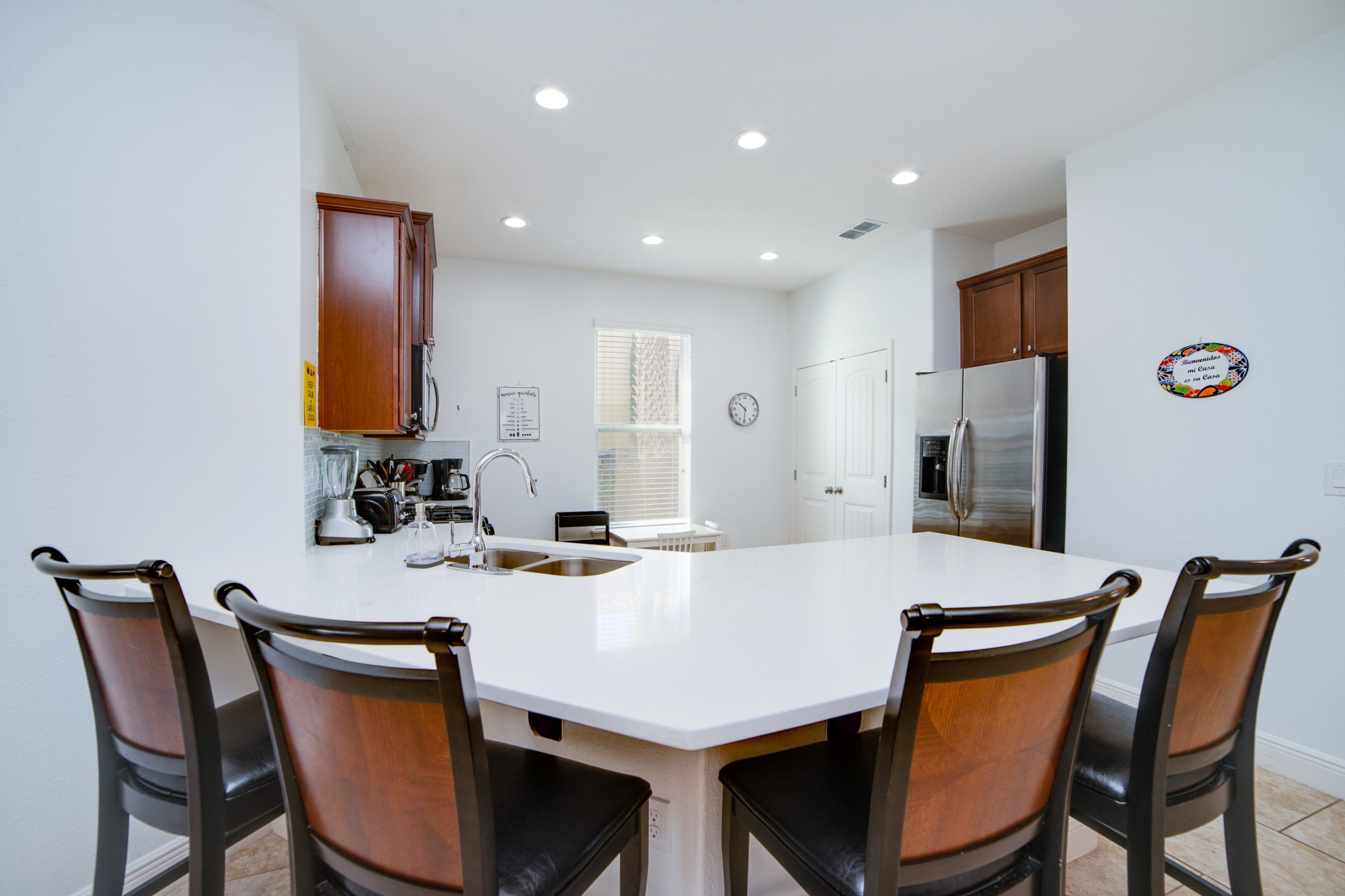 A kitchen with a central island, four chairs, a refrigerator, and wooden cabinets.