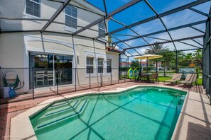 A pool area with a clear view of the pool, a covered patio with chairs, and a house in the background. - 4 Bedroom Townhouse with Pool (Kissimmee)