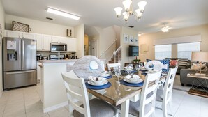 A modern kitchen with white cabinets, stainless steel appliances, and a dining area with a glass table and white chairs. - 4 Bedroom Townhouse with Pool (Kissimmee)