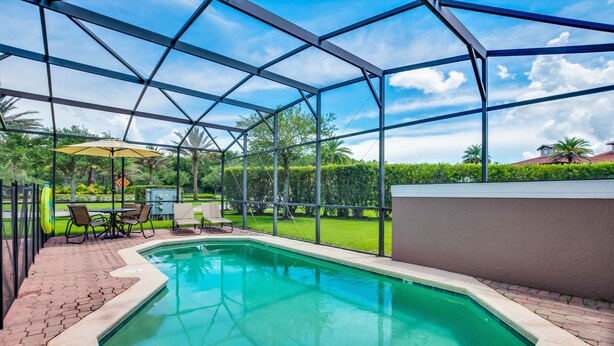 A swimming pool with a glass enclosure, surrounded by a patio area with chairs and a table. - 4 Bedroom Townhouse with Pool (Kissimmee)
