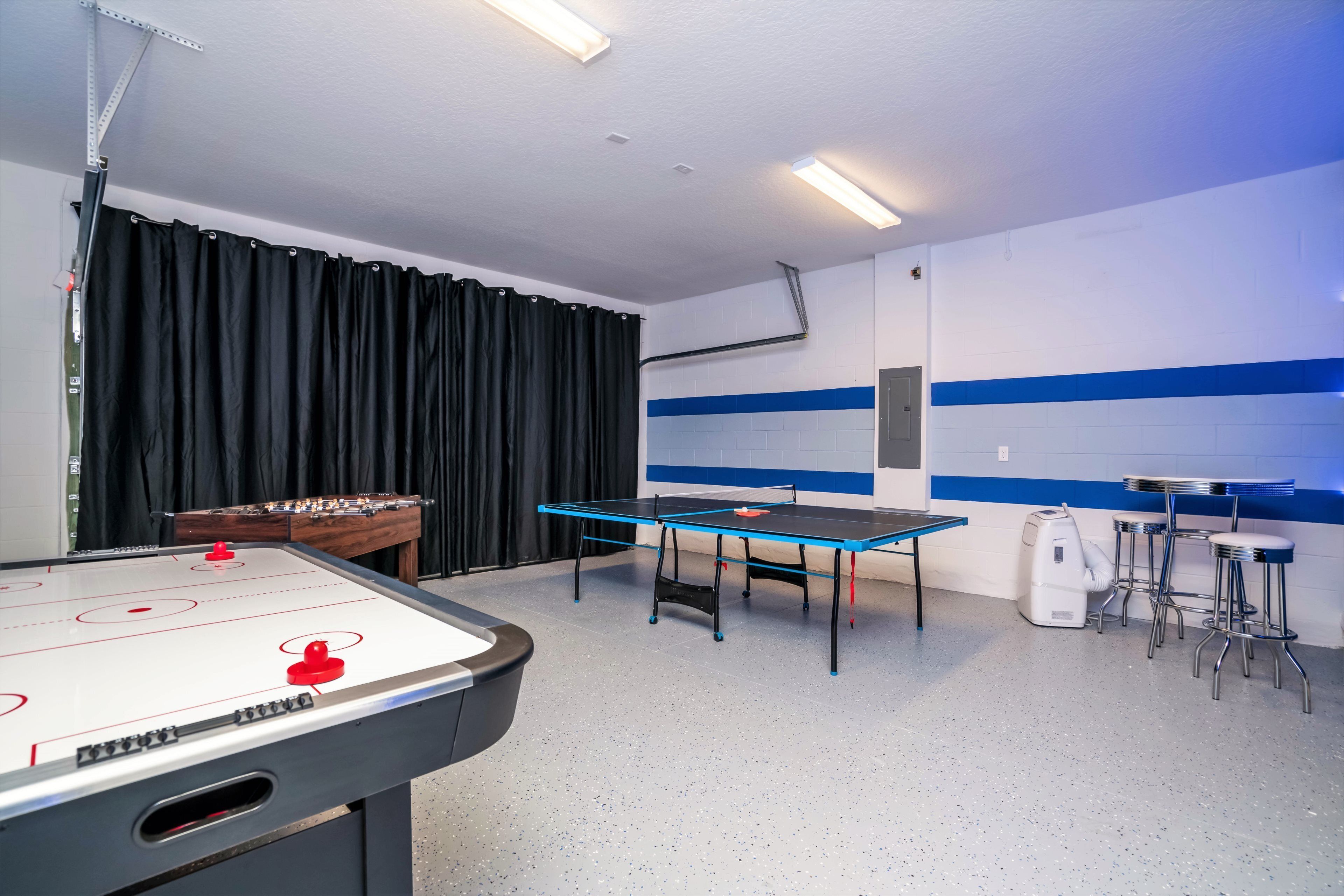 A room with a foosball table, a ping pong table, and a foosball table with a red ball.