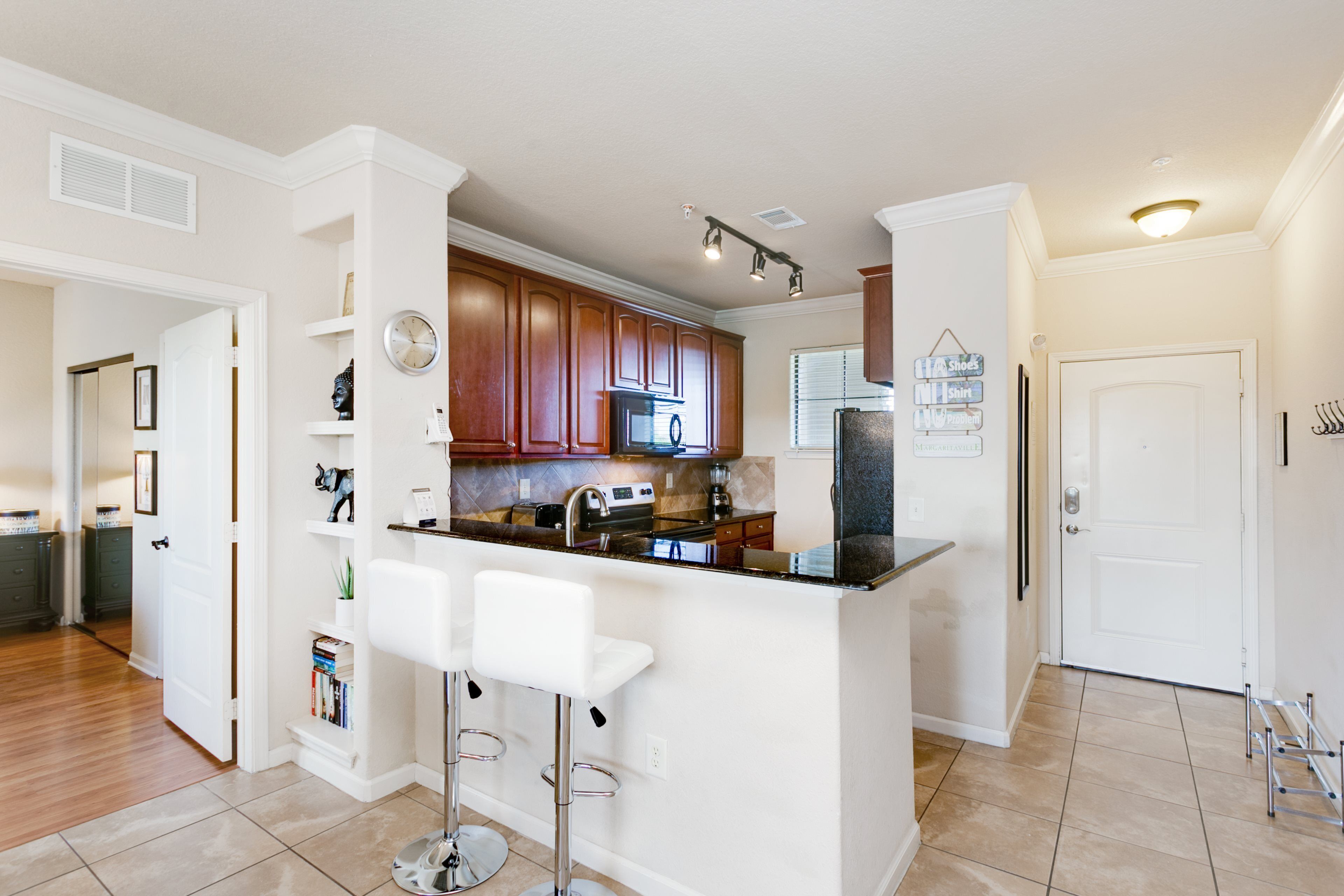 A modern kitchen with a central island, bar stools, wooden cabinets, and stainless steel appliances.